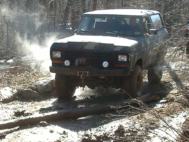 Dark off-road vehicle with winch, driving through mud and kicking up dust