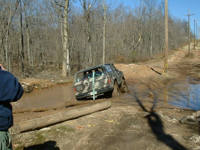 Rear view of a 2003 Jeep Wrangler driving through mud on a wooded trail