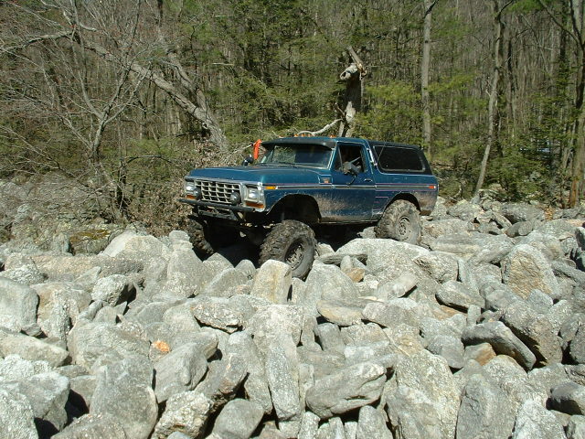 Blue 1978 Ford Bronco with large tires navigating a rocky terrain