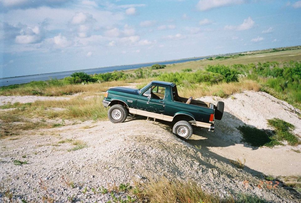 Green Ford Bronco with spare tire on rear, driving on a dirt hill