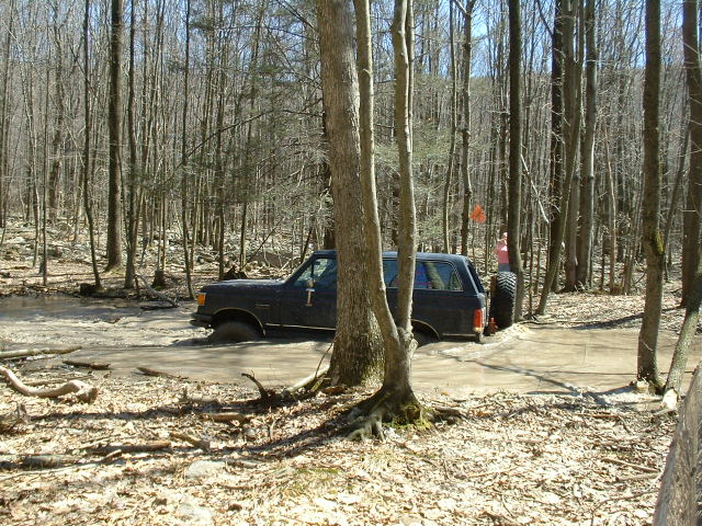 Dark SUV stuck in mud, side view. Appears to be a Ford Bronco II
