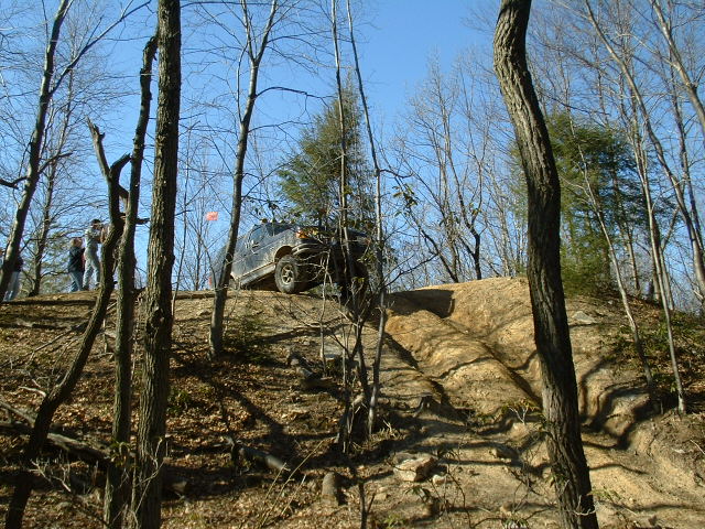 Dark SUV on a dirt hill, with people watching. The vehicle appears to be from the early 2000s