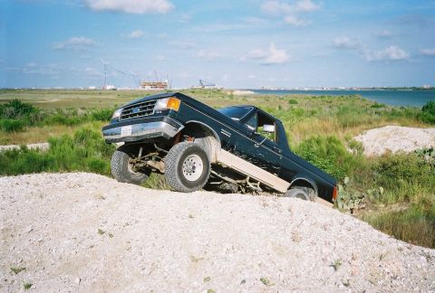 1990 Ford Bronco - This dark pickup truck, likely from the late 1980s, is navigating a challenging dirt terrain.