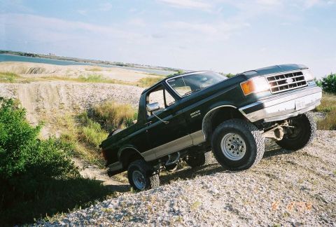 1990 Ford Bronco - This 1990 Ford Bronco navigates off-road terrain on a sandy incline under a bright sky.