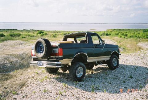 1990 Ford Bronco - Rear view of a 1990 Ford Bronco parked on a dirt and gravel area with a body of water behind it.