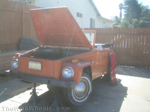 1990 Ford Bronco - orange Volkswagen Thing convertible with its front hood raised sits on jack stands in a wood-fenced backyard.