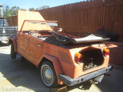 1990 Ford Bronco - rear of a disassembled orange Volkswagen Thing shows its open engine lid, amber taillights and folded soft top in a yard.