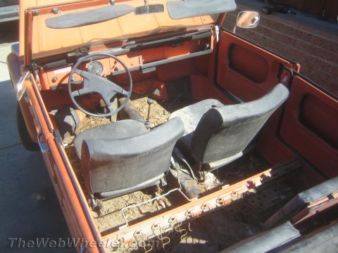 1990 Ford Bronco - interior of an orange Volkswagen Thing shows a thin steering wheel, floor shifter and two worn gray bucket seats.