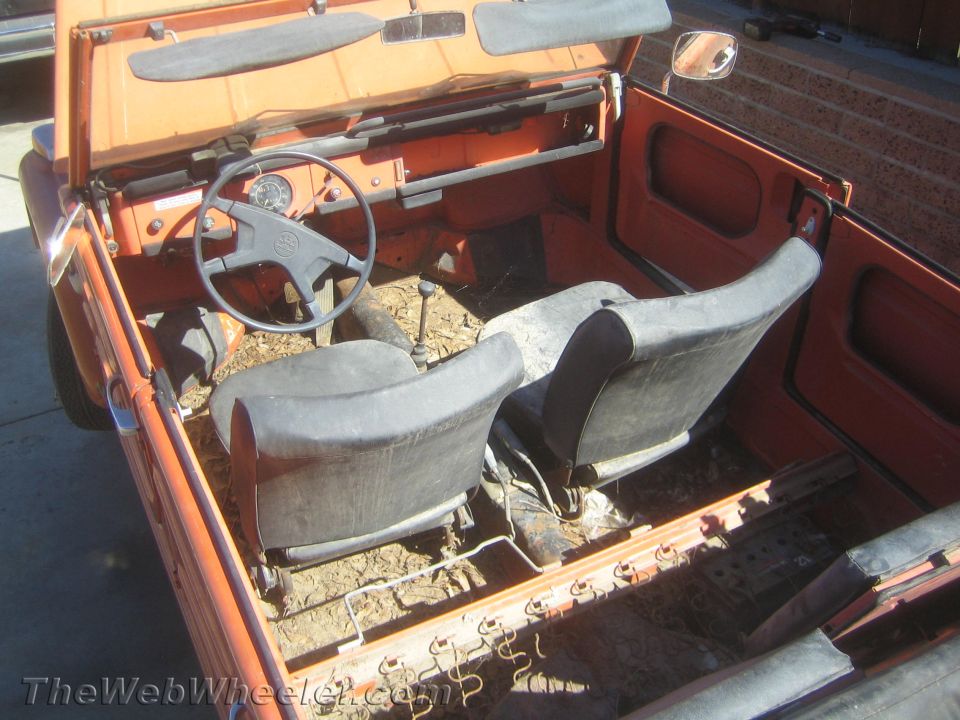 Interior of orange VW Thing with steering wheel, shifter and two gray bucket seats