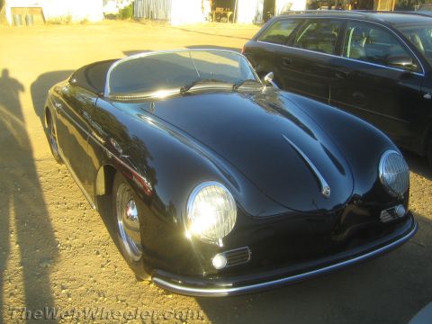 1990 Ford Bronco - glossy black Porsche 356 Speedster-style roadster shows its rounded fenders and chrome headlights in a dirt yard at dusk.