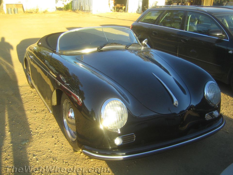 Front three-quarter of black Porsche 356 Speedster-style roadster in a yard at dusk