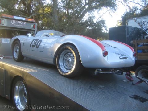 1990 Ford Bronco - silver Porsche 550-style spyder numbered 130 with a red rear stripe sits on a flatbed truck among trees.