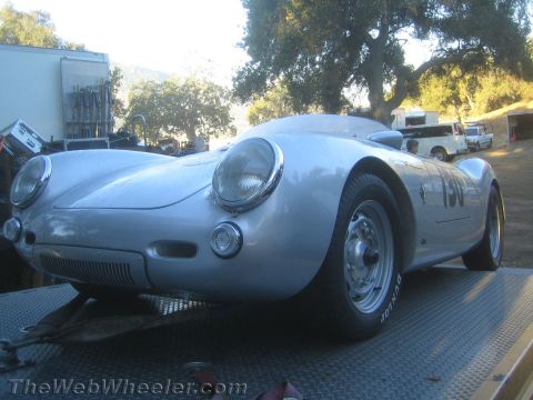 1990 Ford Bronco - silver Porsche 550-style spyder numbered 130 shows its low rounded nose and headlights while loaded on a flatbed among trees.