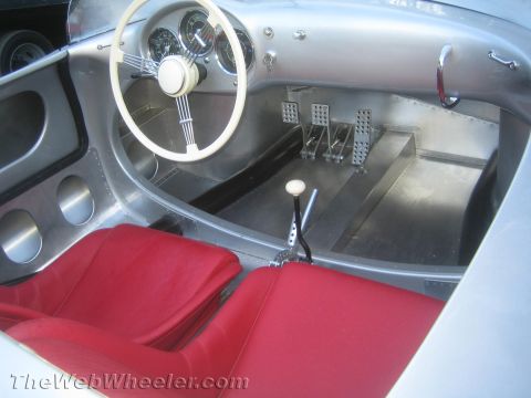 1990 Ford Bronco - Interior of a silver vintage racing roadster showing a white steering wheel, gauges, drilled alloy pedals and red bucket seats.