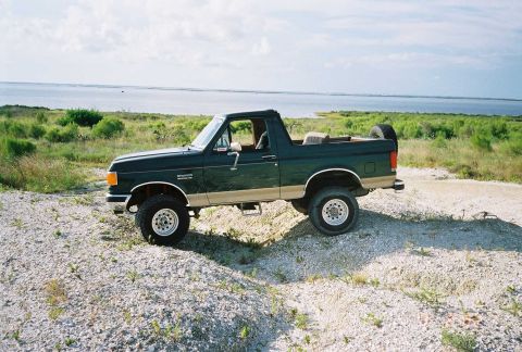 1990 Ford Bronco - This Ford Bronco is parked off-road near a body of water.