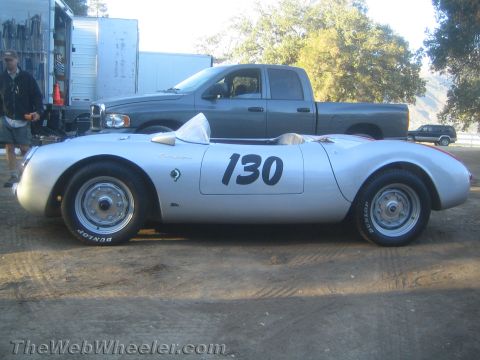 1990 Ford Bronco - Side profile of a silver vintage open racing roadster numbered 130, riding on Dunlop tires beside a pickup truck.