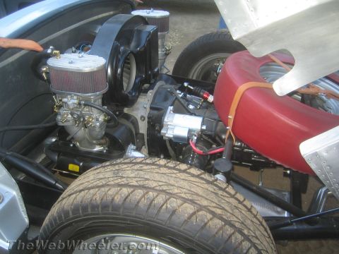 1990 Ford Bronco - Rear engine bay of a vintage roadster showing dual carburetors with air filters, a starter motor and a red-painted spare wheel.