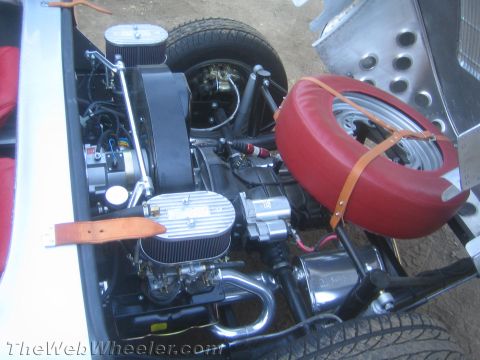 1990 Ford Bronco - Detailed view of a roadster's rear engine bay with twin air-filtered carburetors, chrome headers and a leather-strapped red spare wheel.