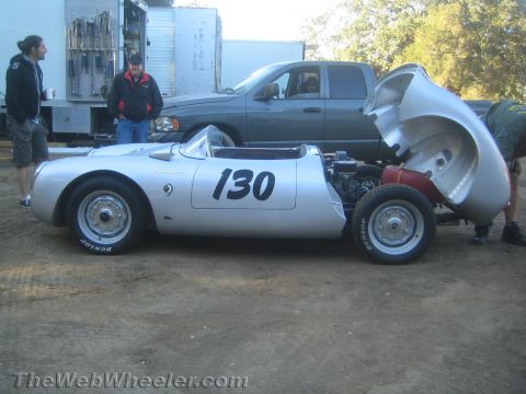 1990 Ford Bronco - Silver vintage racing roadster numbered 130 with its rear clamshell bodywork lifted, as two men look on in a dirt paddock.