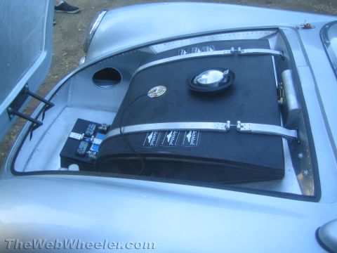 1990 Ford Bronco - Open front compartment of a silver vintage roadster housing a black strapped tank or fuel cell and a battery.