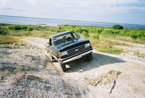 1990 Ford Bronco - This 1990 Ford Bronco is navigating a rough dirt path with a lake in the background.