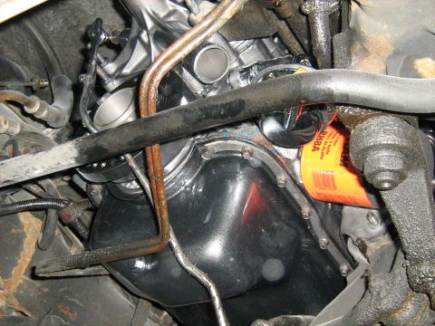 1988 Mercury Grand Marquis - Close-up view of an engine's oil pan and an orange oil filter, with visible plumbing and suspension components.