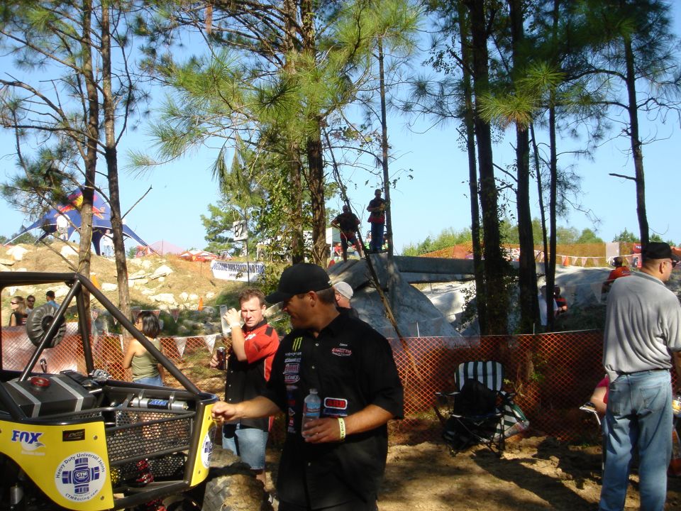 Yellow tube-chassis rock buggy with FOX decals in the pits as crew and spectators stand nearby