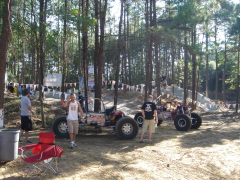 2002 Jeep Wrangler - Custom off-road vehicles are staged in a wooded area with spectators and event banners visible.