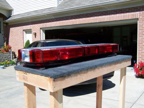 2003 Ford Crown Victoria - An emergency light bar is displayed on a wooden stand in front of a garage.