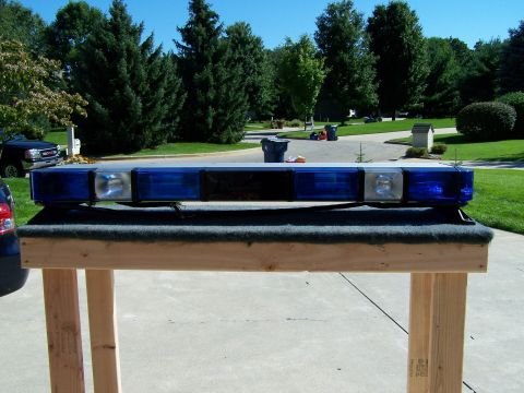 2003 Ford Crown Victoria - A light bar with blue and clear lenses is displayed on a table in front of a suburban background.