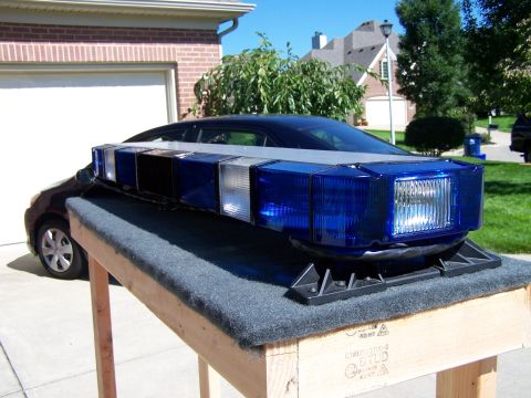 2003 Ford Crown Victoria - A blue emergency light bar is mounted on the roof of a dark sedan, displayed outdoors.
