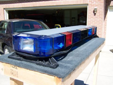 2003 Ford Crown Victoria - Police light bar with blue and red lenses sits on a stand, with a car in the garage behind it.