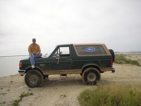 1990 Ford Bronco - Man sits on the hood of a 1990 Ford Bronco parked by the water.