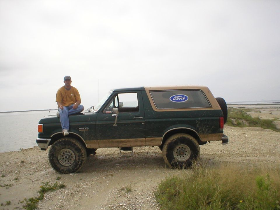 Two-tone green and tan full-size Ford Bronco parked on a sandy shoreline
