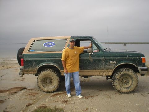 1990 Ford Bronco - A man poses with a muddy green Ford Bronco, a two-tone tan roof and off-road tires.