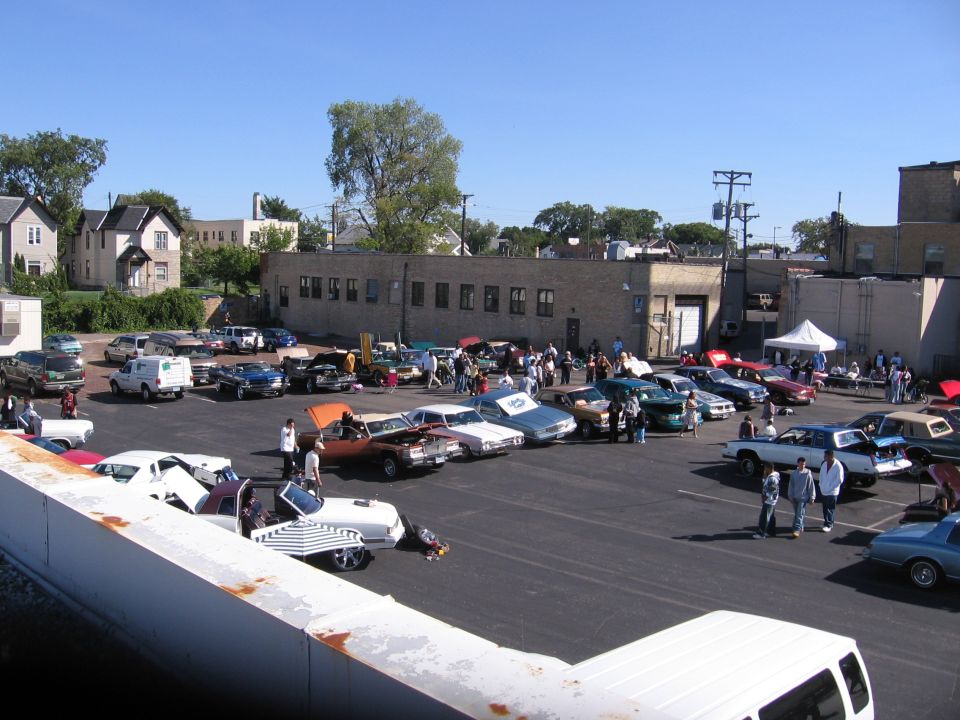 Outdoor car show with many vehicles parked in a lot under a clear blue sky