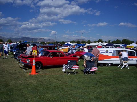1972 Ford Ranchero - A red coupe and an ambulance are on display at an outdoor car show under a blue sky with clouds.