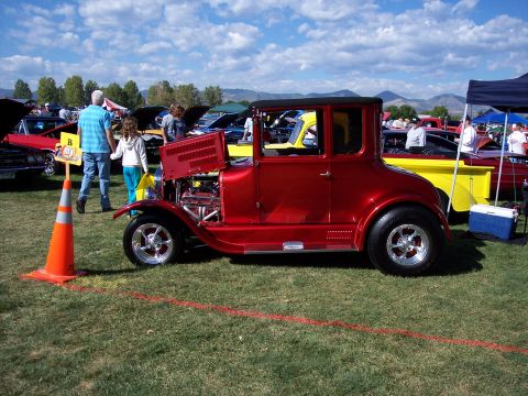 1972 Ford Ranchero - A red coupe hot rod is displayed at an outdoor car show with other vehicles and spectators.
