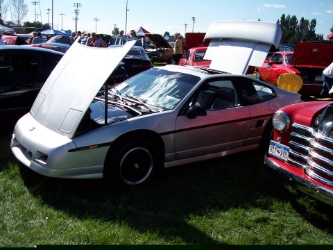 1972 Ford Ranchero - Silver Pontiac Fiero on display at an outdoor car show, hood open to reveal the engine bay.
