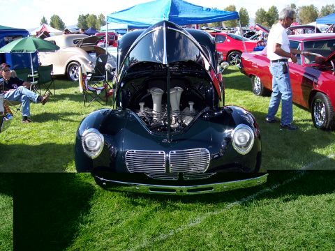 1972 Ford Ranchero - A black hot rod with its hood open, revealing the engine, sits on display at an outdoor car show.