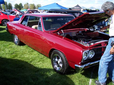 1972 Ford Ranchero - A man inspects the engine of a shiny red coupe at an outdoor car show with other vehicles and tents visible.