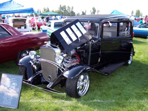 1972 Ford Ranchero - A black hot rod is displayed with its hood open, revealing the engine, at an outdoor car show.