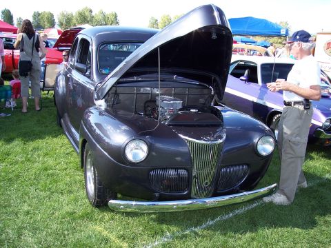 1972 Ford Ranchero - A classic car show features a dark gray coupe with its hood raised, revealing the engine compartment.