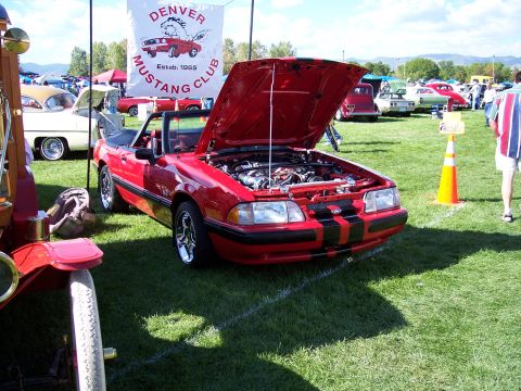1972 Ford Ranchero - A red convertible is displayed with its hood open at a car show, with other vehicles and a banner in the background.