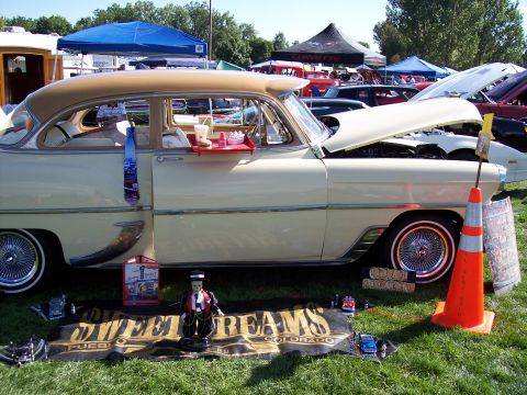 1972 Ford Ranchero - A vintage sedan, likely a 1954 model, is displayed at an outdoor car show with a food tray attached to its door.