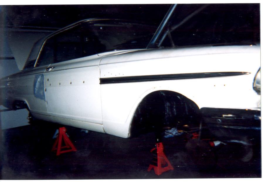 White 1964 Ford Fairlane hardtop on red jack stands in a garage, wheels removed, side view