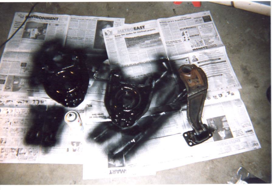 Freshly black spray-painted suspension control arms drying on newspaper on a garage floor