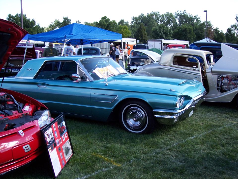 Teal 1960 Ford Thunderbird parked next to a silver coupe and a red car with its hood up
