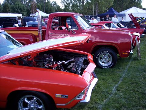 1972 Ford Ranchero - A red pickup truck and a red car with its hood open are displayed at an outdoor car show.