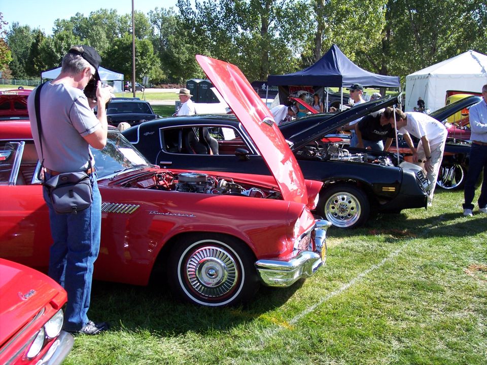 Red 1957 Ford Thunderbird with hood open, parked on grass at car show